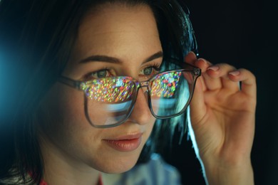 Photo of Young woman wearing glasses with reflection on dark background, closeup