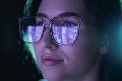 Photo of Young woman wearing glasses with reflection on dark background, closeup
