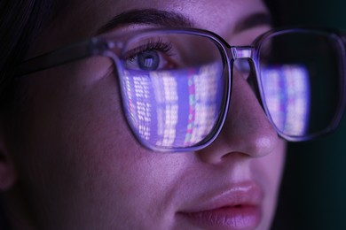 Photo of Young woman wearing glasses with reflection on dark background, closeup