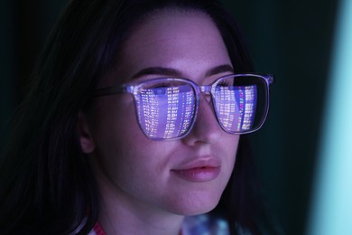 Photo of Young woman wearing glasses with reflection on dark background, closeup