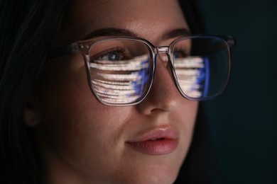 Photo of Young woman wearing glasses with reflection on dark background, closeup