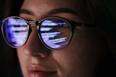 Photo of Young woman wearing glasses with reflection on dark background, closeup