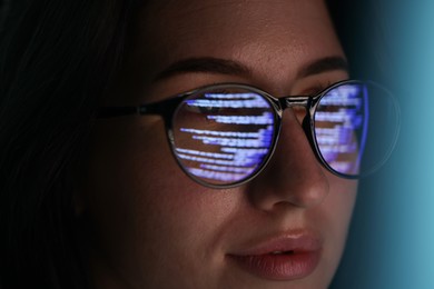 Photo of Young woman wearing glasses with reflection on dark background, closeup