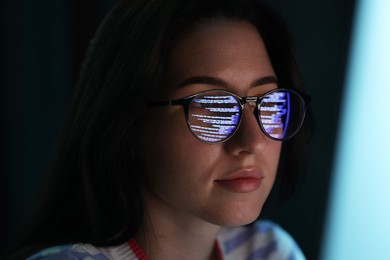 Photo of Young woman wearing glasses with reflection on dark background, closeup