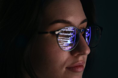 Photo of Young woman wearing glasses with reflection on dark background, closeup