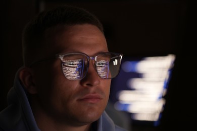 Photo of Young man wearing glasses with reflection on dark background, closeup