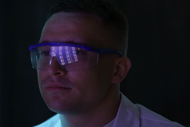 Photo of Young man wearing glasses with reflection on dark background, closeup