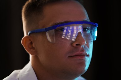 Photo of Young man wearing glasses with reflection on dark background, closeup