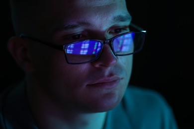 Photo of Young man wearing glasses with reflection on dark background, closeup