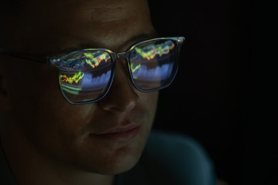 Photo of Young man wearing glasses with reflection on dark background, closeup