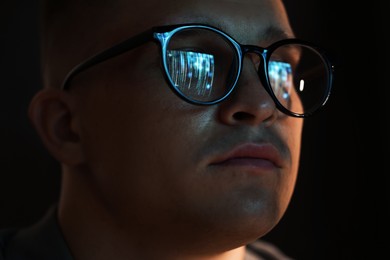 Photo of Young man wearing glasses with reflection on dark background, closeup