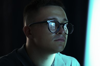 Photo of Young man wearing glasses with reflection on dark background, closeup