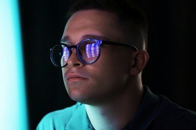 Photo of Young man wearing glasses with reflection on dark background, closeup