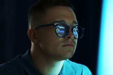 Photo of Young man wearing glasses with reflection on dark background, closeup