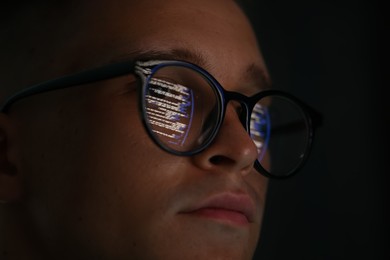 Photo of Young man wearing glasses with reflection on dark background, closeup