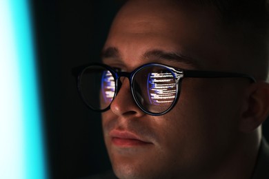 Photo of Young man wearing glasses with reflection on dark background, closeup