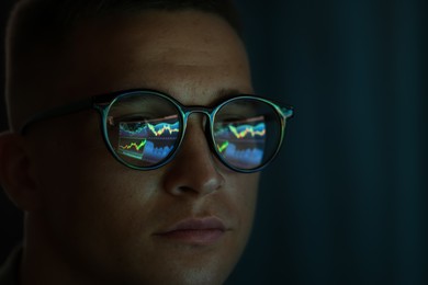 Photo of Young man wearing glasses with reflection on dark background, closeup