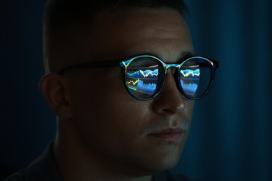 Photo of Young man wearing glasses with reflection on dark background, closeup