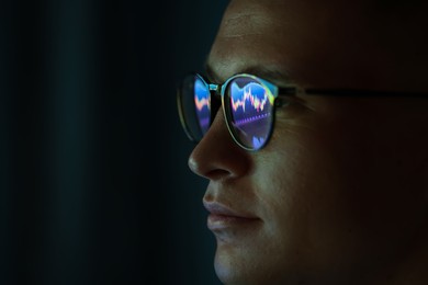 Photo of Young man wearing glasses with reflection on dark background, closeup