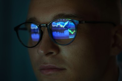 Photo of Young man wearing glasses with reflection on dark background, closeup