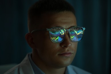 Photo of Young man wearing glasses with reflection on dark background, closeup