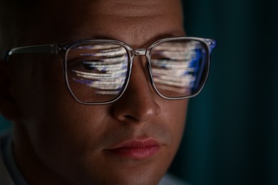 Photo of Young man wearing glasses with reflection on dark background, closeup