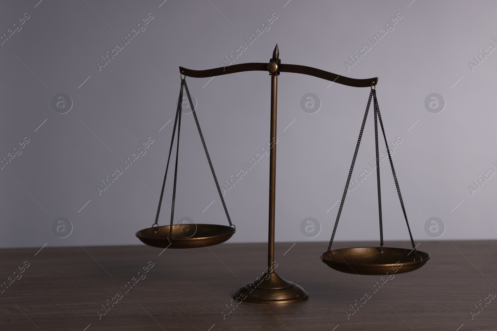 Scales of justice on wooden table against grey background Photo of Scales of justice on wooden table against grey background
