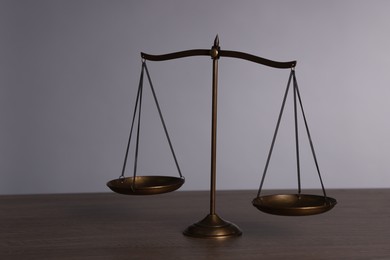 Photo of Scales of justice on wooden table against grey background