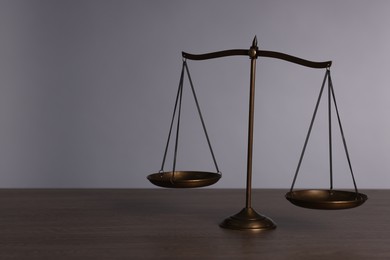 Photo of Scales of justice on wooden table against grey background. Space for text