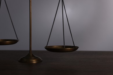 Photo of Scales of justice on wooden table against grey background, closeup
