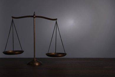 Photo of Scales of justice on wooden table against grey background. Space for text