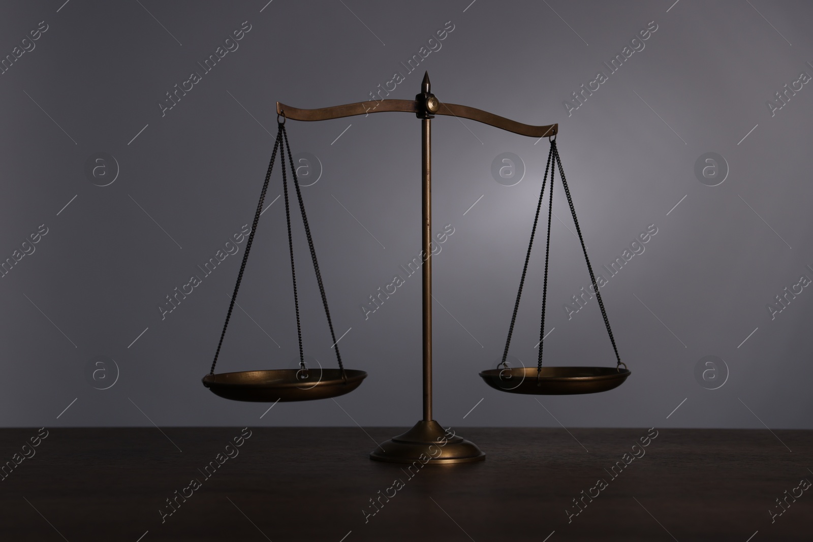 Scales of justice on wooden table against grey background Photo of Scales of justice on wooden table against grey background