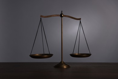 Photo of Scales of justice on wooden table against grey background