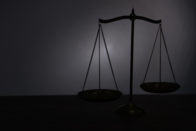 Photo of Scales of justice on table in darkness. Space for text