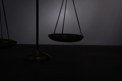 Photo of Scales of justice on table in darkness, closeup
