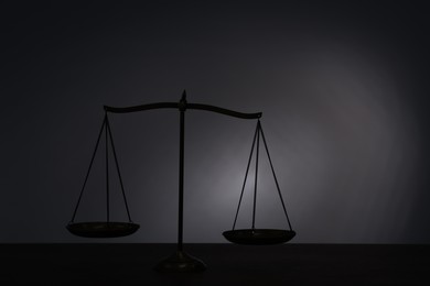 Photo of Scales of justice on table in darkness. Space for text