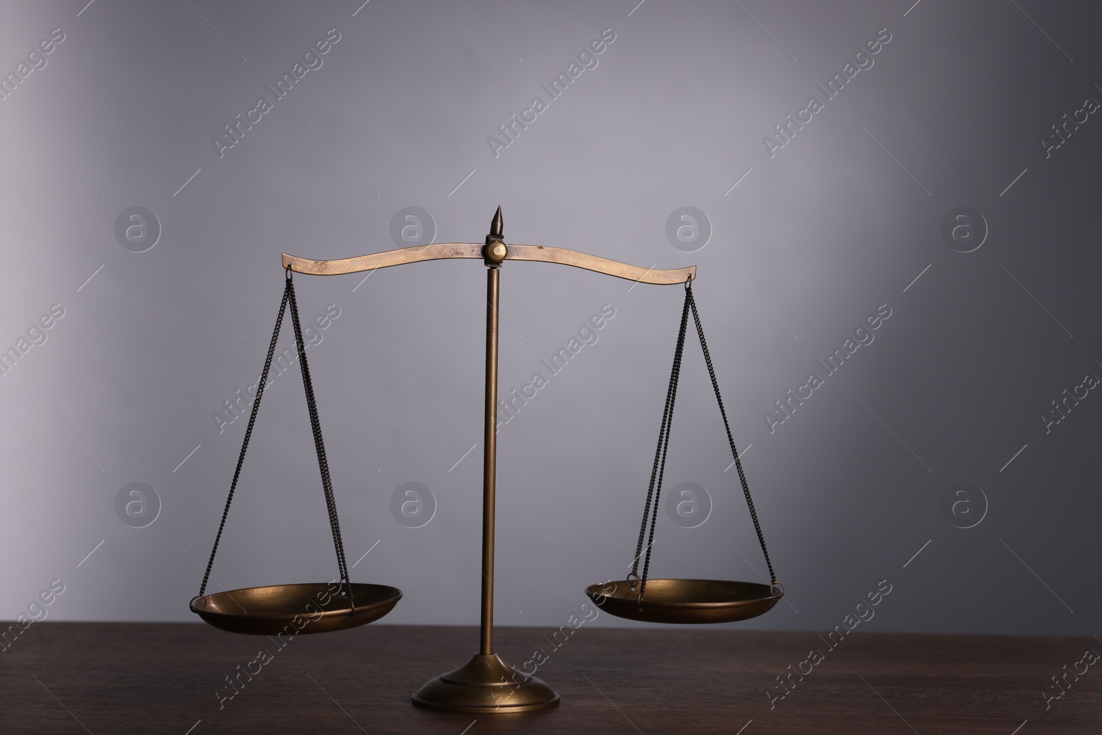 Photo of Scales of justice on wooden table against grey background