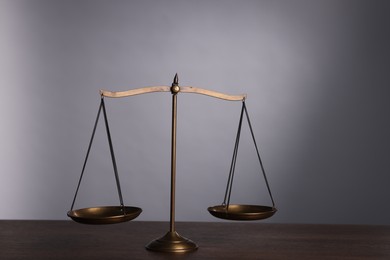 Photo of Scales of justice on wooden table against grey background
