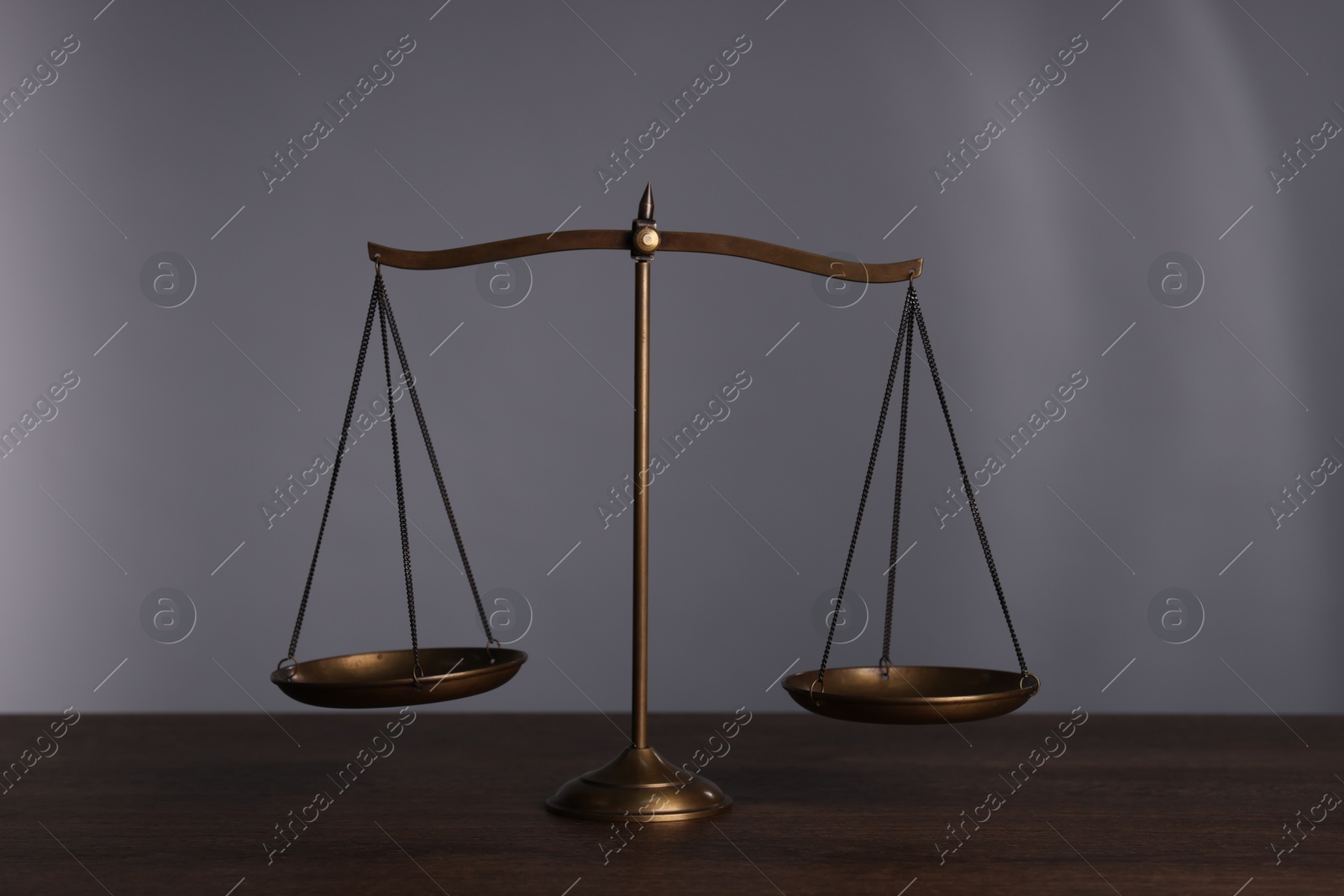 Photo of Scales of justice on wooden table against grey background