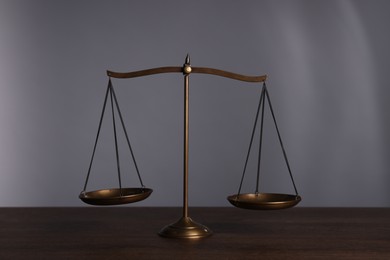 Photo of Scales of justice on wooden table against grey background