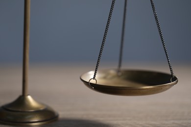 Photo of Scales of justice on wooden table against grey background, closeup