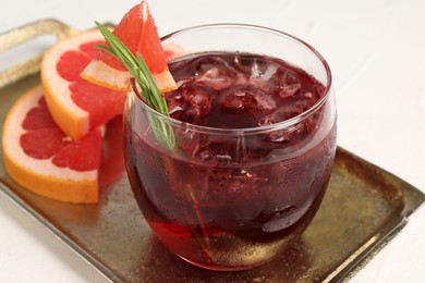 Photo of Tasty cocktail with grapefruit, ice cubes and rosemary on white table, closeup