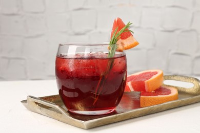Photo of Tasty cocktail with grapefruit, ice cubes and rosemary on white table, closeup
