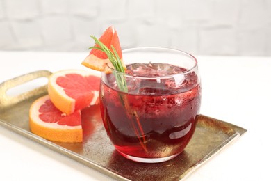 Photo of Tasty cocktail with grapefruit, ice cubes and rosemary on white table, closeup