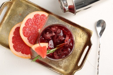 Photo of Tasty cocktail with grapefruit, ice cubes, rosemary and shaker on white table, flat lay