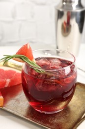 Photo of Tasty cocktail with grapefruit, ice cubes, rosemary and shaker on white table, closeup