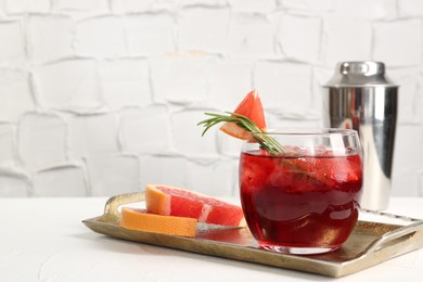 Photo of Tasty cocktail with grapefruit, ice cubes, rosemary and shaker on white table, closeup. Space for text