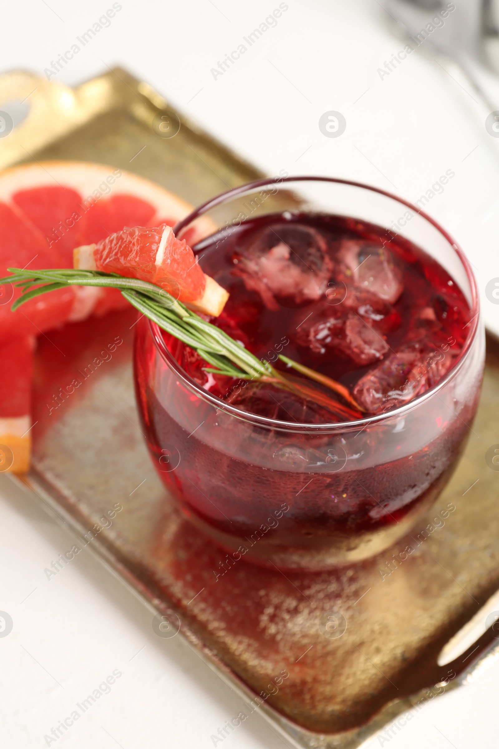 Photo of Tasty cocktail with grapefruit, ice cubes and rosemary on white table, closeup