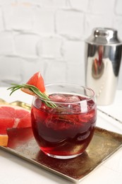 Photo of Tasty cocktail with grapefruit, ice cubes, rosemary and shaker on white table, closeup