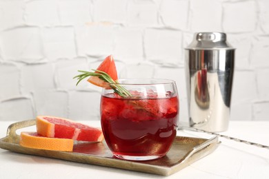 Photo of Tasty cocktail with grapefruit, ice cubes, rosemary and shaker on white table, closeup